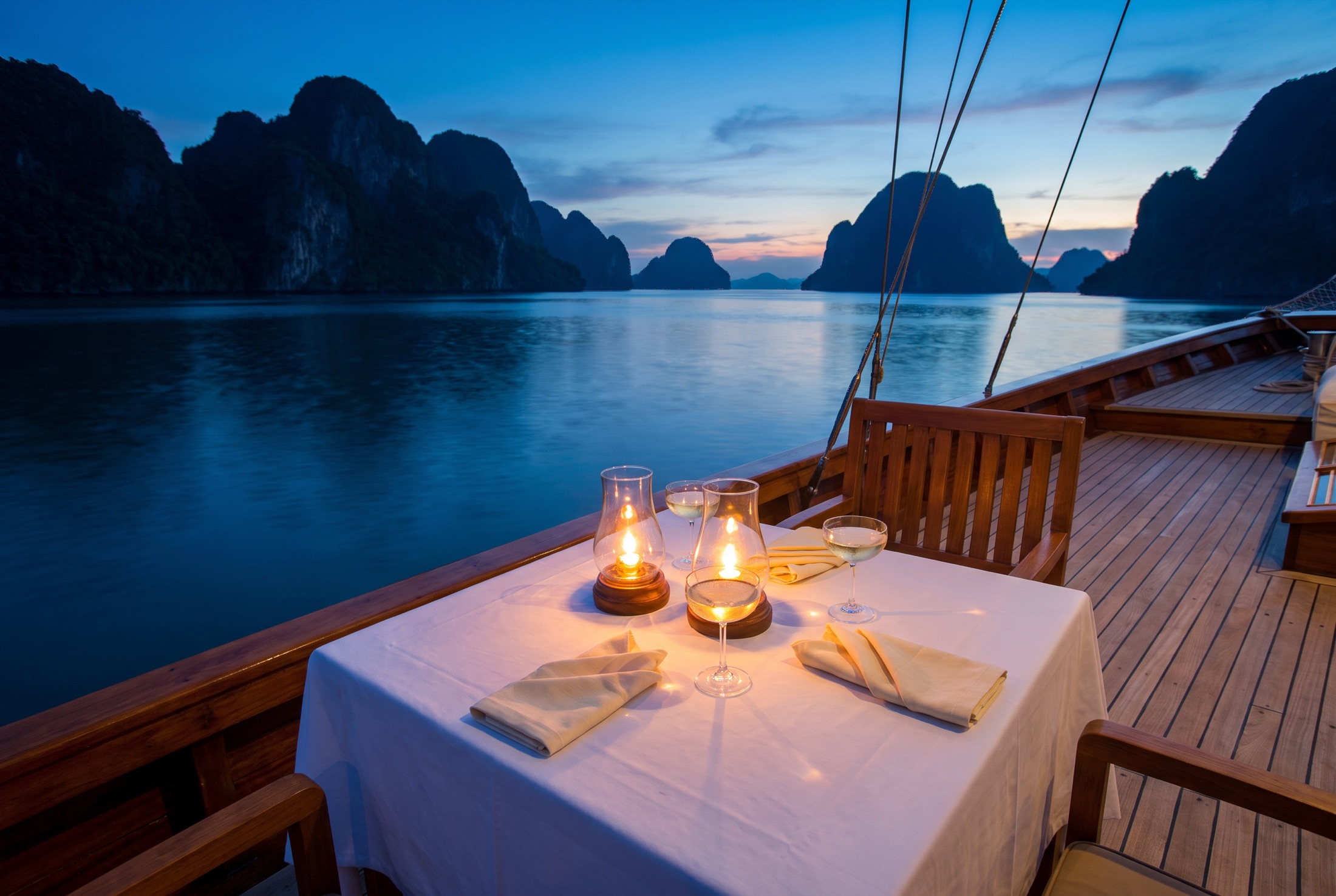 A candlelit dinner for two on the deck of a classic yacht among limestone islands at blue hour
